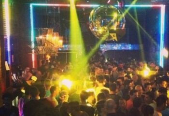 Gay men's travel advice: A crowded gay club, possibly SCORE, with a disco ball, stage lights, and a large group of people dancing.