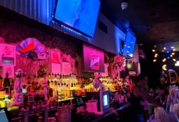 Nathan's Beach Club bar interior at night. Colorful bottles line the shelves, with screens above. Gay travel destination. 4-25.jpg