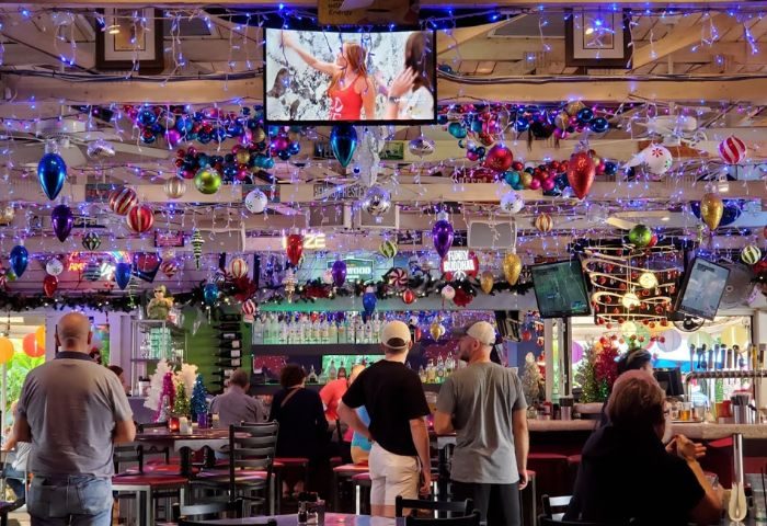 Interior of Rosie's Bar & Grill, a gay bar, with patrons. Festive decorations, TV screens, and bar setting. Gay travel destination.