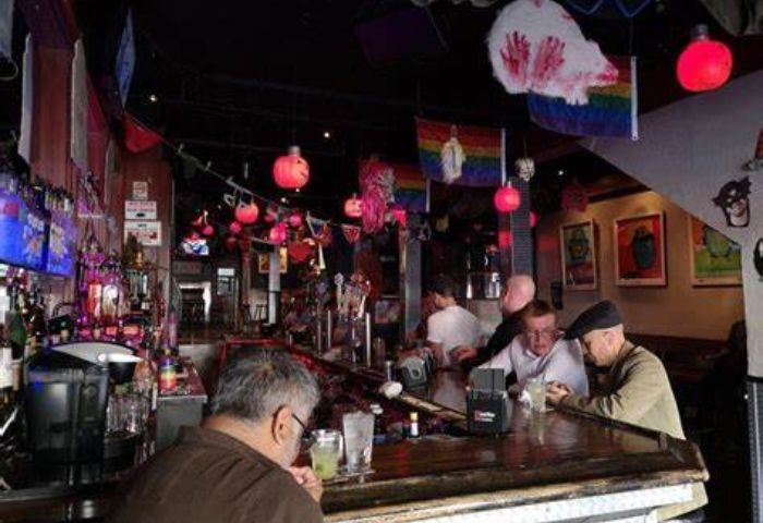 Interior view of a Castro gay bar in San Francisco. Rainbow flags, red lanterns, and patrons at the bar create a lively atmosphere.
