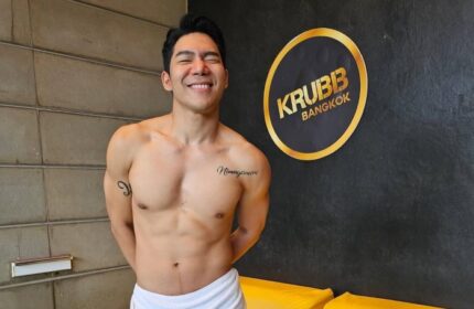 Shirtless man smiling in front of the Krubb Bangkok logo. Gay travel in Bangkok. Krubb is a gay sauna in Bangkok.