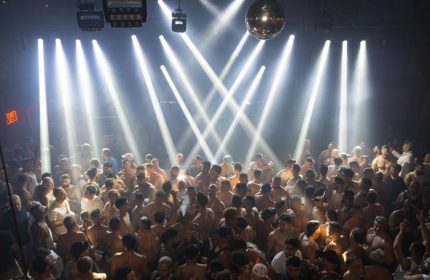 Gay Industry party: A large, shirtless crowd of men dancing under bright lights and a disco ball. Gay travel advice, nightlife.