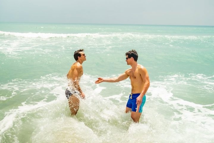 Gay couple in ocean at Vana Belle, a Luxury Collection Resort in Koh Samui, Thailand. Men's swimwear fashion on tropical beach.