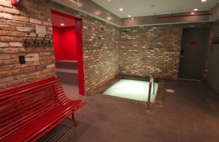 Gaythering Sauna interior. Brick walls, red bench, and a small pool. A doorway leads to a red room. Gay travel advice. 5-17.jpg.