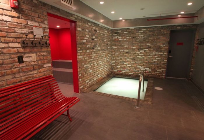 Gaythering Sauna interior. Brick walls, red bench, and a small pool. A doorway leads to a red room. Gay travel advice. 5-17.jpg.
