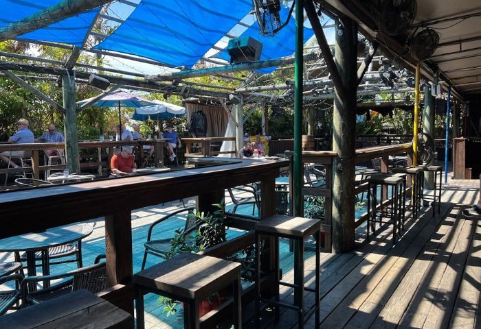 Outdoor seating area at Scandals Saloon, a popular gay bar. Wooden deck, bar stools, blue awning. 5-2.jpg. Gay men travel.