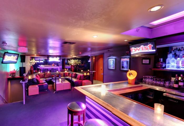 Interior of Twist, a gay bar. Purple lighting, bar counter, lounge seating, TVs, and bottles. Gay travel advice.