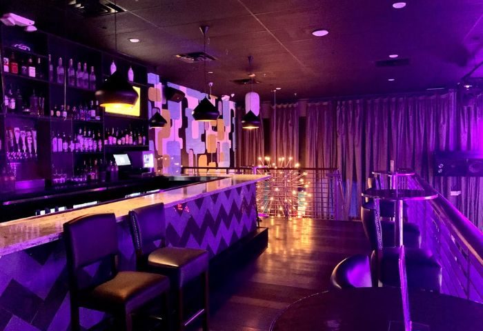 Hunters Wilton Manors bar area with purple lighting. Bar stools, liquor bottles, and a decorative wall. Gay bar & nightlife. 5-4.jpg