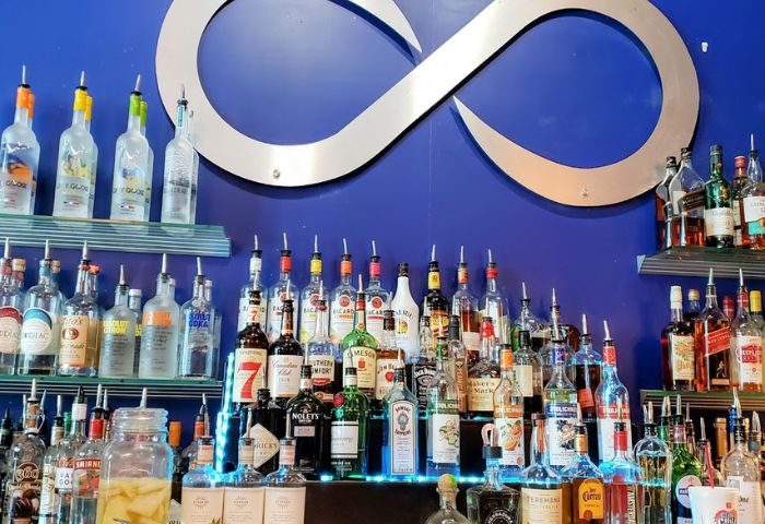 Infinity Lounge bar interior. Backlit shelves display liquor bottles against a blue wall with an infinity symbol. Gay travel advice.