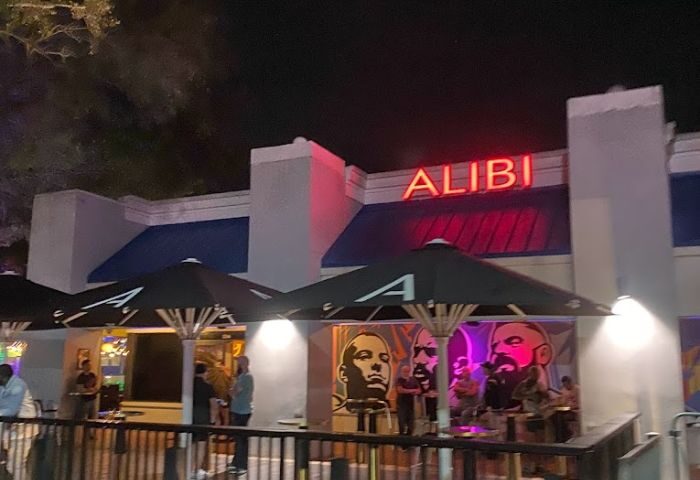 Georgie's ALIBI Monkey Bar exterior at night. Gay bar with neon sign, umbrellas, and people. Gay travel destination. 5-7.jpg