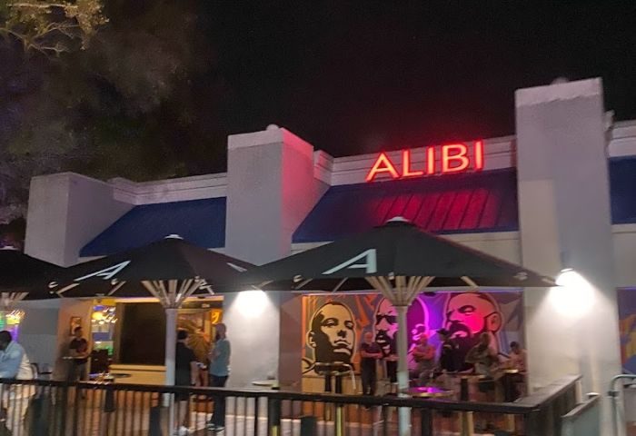 Georgie's ALIBI Monkey Bar exterior at night. Gay bar with neon sign, umbrellas, and people. Gay travel destination. 5-7.jpg