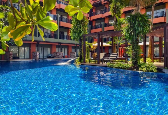 Courtyard Phuket, Patong Beach Resort pool view. Blue tiled pool, lounge chairs, and tropical plants. Ideal gay travel destination in Thailand.