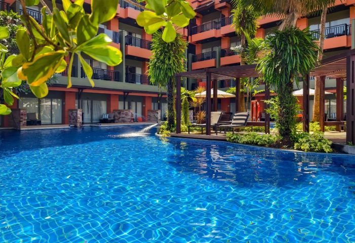 Courtyard Phuket, Patong Beach Resort pool view. Blue tiled pool, lounge chairs, and tropical plants. Ideal gay travel destination in Thailand.