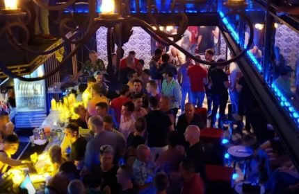 Gay party at a strip bar in Puerto Vallarta, Mexico. Men are drinking and socializing in a crowded, dimly lit space.