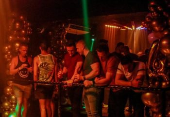 Gay party in Puerto Vallarta's strip bar. Men enjoy drinks at a bar during a gay party with balloons and colorful lights.