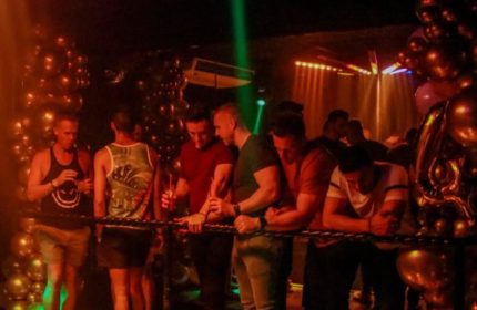 Gay party in Puerto Vallarta's strip bar. Men enjoy drinks at a bar during a gay party with balloons and colorful lights.