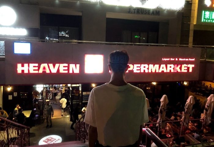 Heaven Beer Bar: Man stands before the Heaven Supermarket entrance, a gay-friendly liquor bar and Mexican food spot. Nightlife scene.