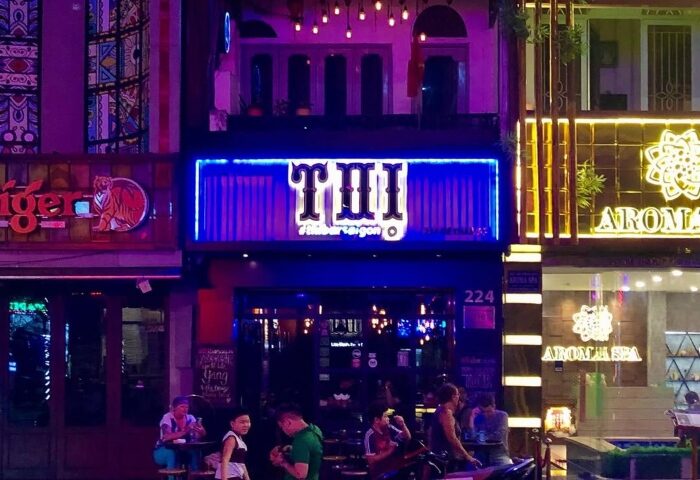 Thi Bar in Vietnam. Gay travel advice. Night view of the bar with neon lights and people sitting outside. Saigon nightlife.
