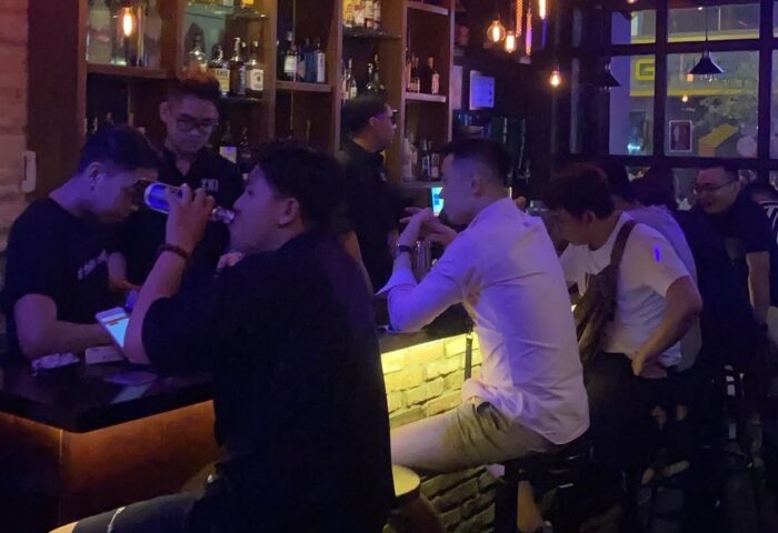 Thi Bar scene. Gay men at a bar, drinking and socializing. Nightlife in a gay travel destination. Bar with bottles on shelves.