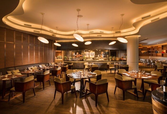 Opus Grill at voco Orchard Singapore, an IHG Hotel. Fine dining restaurant with modern decor, tables set, and open kitchen. Gay-friendly travel.