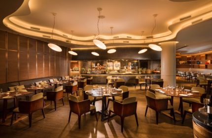 Opus Grill at voco Orchard Singapore, an IHG Hotel. Fine dining restaurant with modern decor, tables set, and open kitchen. Gay-friendly travel.