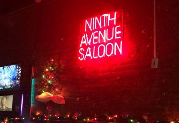 Ninth Avenue Saloon, a gay bar in New York. Red neon sign on a brick wall, Christmas tree, and festive lights. Gay travel advice.