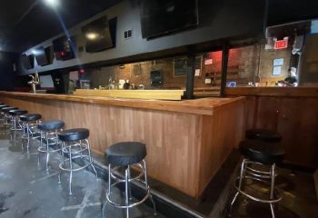 Interior of 9th Avenue Saloon, a gay bar in New York. Bar stools line the counter. TVs are mounted above the bar. Gay travel advice.