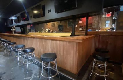 Interior of 9th Avenue Saloon, a gay bar in New York. Bar stools line the counter. TVs are mounted above the bar. Gay travel advice.