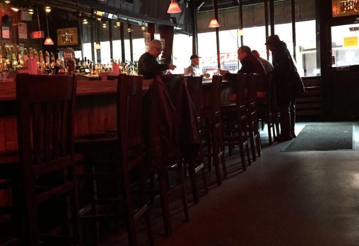 Interior of 9th Avenue Saloon, a gay bar in New York. People sit at the bar. A row of bar stools lines the counter in this NYC gay bar.