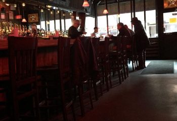 Interior of 9th Avenue Saloon, a gay bar in New York. People sit at the bar. A row of bar stools lines the counter in this NYC gay bar.