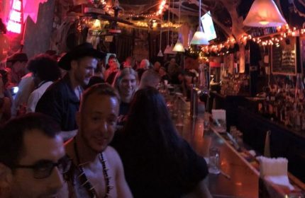 Interior of 9th Avenue Saloon, a gay bar in New York City, decorated for Halloween. Patrons are standing at the bar, enjoying drinks.