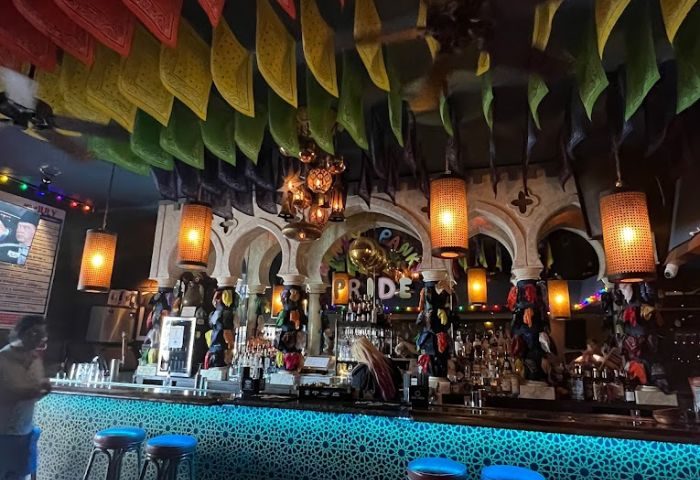 Akbar Drinks: Interior of gay bar with rainbow flags, ornate arches, and colorful lighting. A popular gay travel destination for drinks.