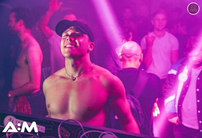 A:M Afterhours at Protocol, London's hottest gay dance club. Shirtless man smiles in a crowded after-hours gay club with purple lighting.