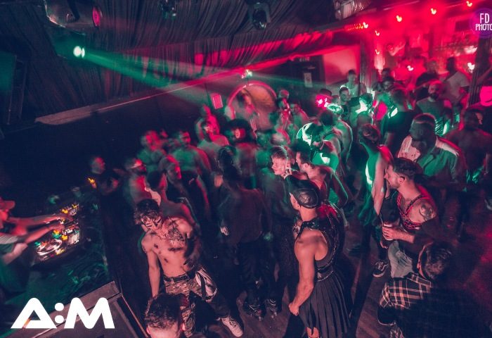 A:M Afterhours at Protocol, Vauxhall's hottest gay after-party in London. Crowd of gay men dancing, red and green lights, DJ booth.