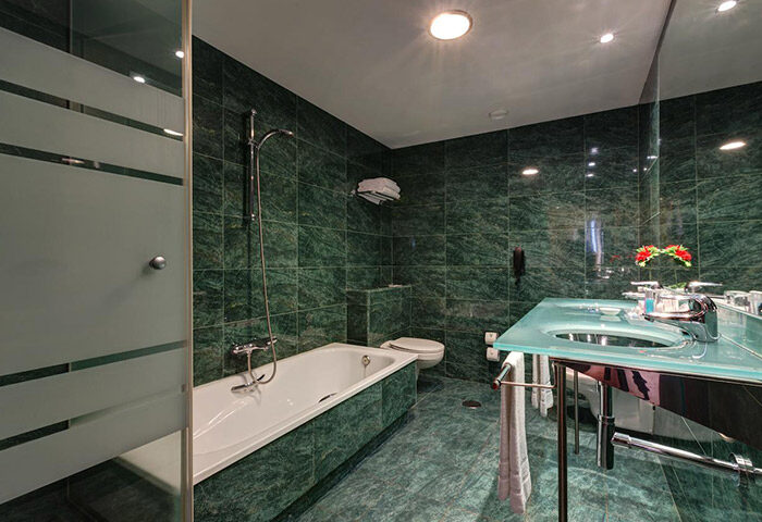 Acevi Villarroel Hotel bathroom. Green marble tiles, bathtub, glass sink. Gay honeymoon hotel in Barcelona's gayborhood. Stylish design.