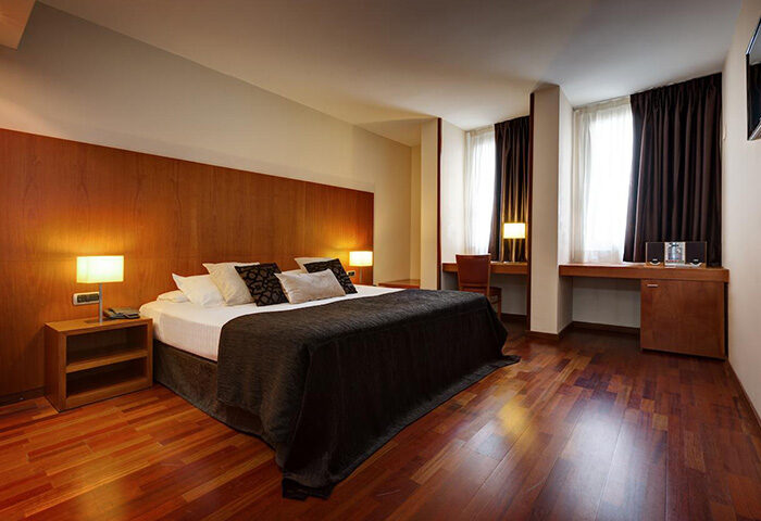 Acevi Villarroel Hotel room in Barcelona's Gayborhood. Features a large bed, wooden floors, and a desk area. Top gay hotel for gay men travel.