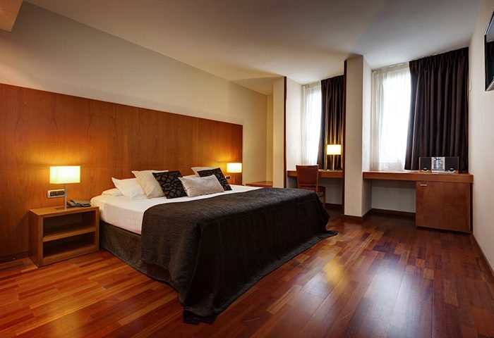 Acevi Villarroel Hotel room in Barcelona's Gayborhood. Features a large bed, wooden floors, and a desk area. Top gay hotel for gay men travel.