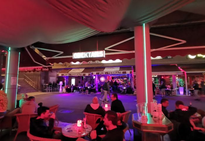 Adonis Bar, a gay bar in Gran Canaria, features a lively outdoor terrace. Patrons sit at tables, enjoying the vibrant nightlife scene.