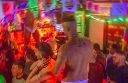 Afterline Milan: Gay men dancing in a crowded, colorful club. Nightlife scene with shirtless men and rainbow decorations. Gay travel advice.