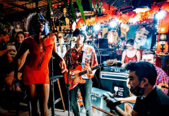 Alcove Koh Phangan beachfront bar: Live music performance at a gay-friendly venue. A drag queen in a red dress stands next to the band.