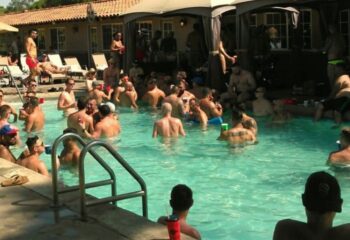 Gay men at All Worlds Resort, Palm Springs. A group of shirtless men are relaxing in a pool at the gay resort, some with drinks in hand.