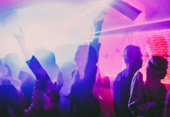 Crowd at AlterEGO Club, Budapest. People dancing, hands raised in the air, enjoying the gay nightlife. Nightclub scene with pink and purple lights.