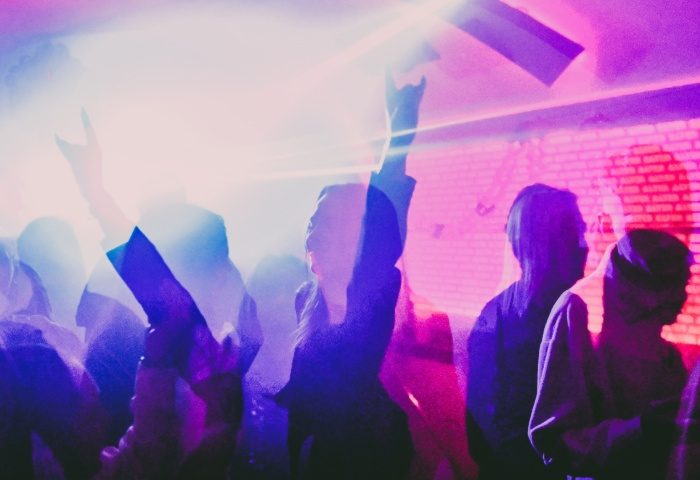 Crowd at AlterEGO Club, Budapest. People dancing, hands raised in the air, enjoying the gay nightlife. Nightclub scene with pink and purple lights.