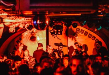 AlterEGO Club Budapest: Gay men celebrate Halloween in costume at a crowded party with red lighting and a disco ball.