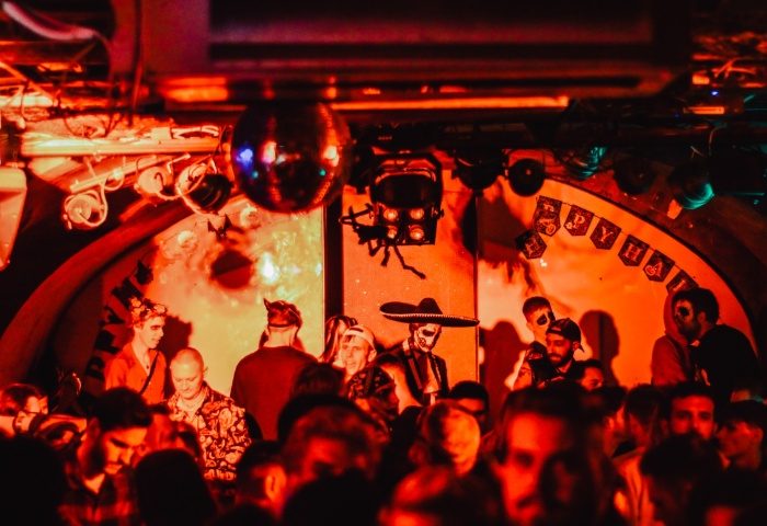 AlterEGO Club Budapest: Gay men celebrate Halloween in costume at a crowded party with red lighting and a disco ball.