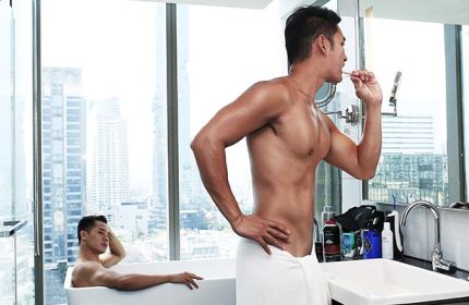 Amara Bangkok Gay Hotel: Two shirtless men in a modern bathroom with city views. One is brushing his teeth, the other relaxing in the bathtub.