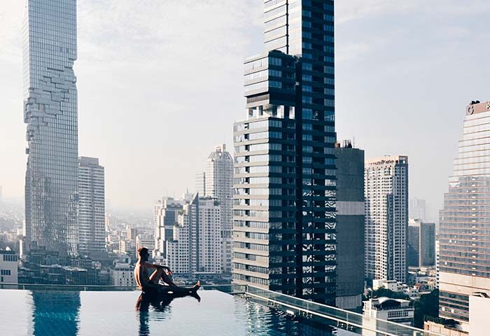 Gay man relaxes at Amara Bangkok Hotel's rooftop pool with city view. Perfect gay travel destination. Modern architecture, luxury, relaxation.