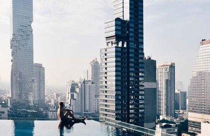 Gay man relaxes at Amara Bangkok Hotel's rooftop pool with city view. Perfect gay travel destination. Modern architecture, luxury, relaxation.