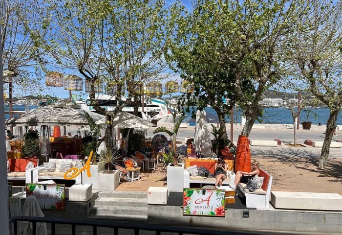 Angelo's Gay Bar in Ibiza: Outdoor seating area with people relaxing on sofas, enjoying the sun and the view of the sea.