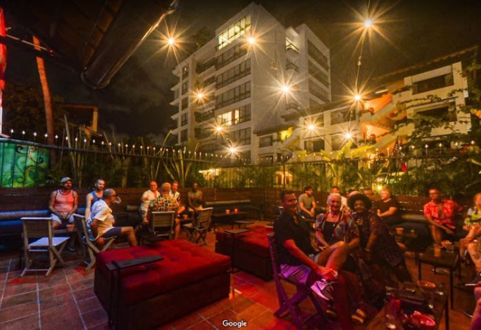 Night view of a gay bar in Puerto Vallarta, Mexico. People are seated in an outdoor patio with red cushions and string lights.